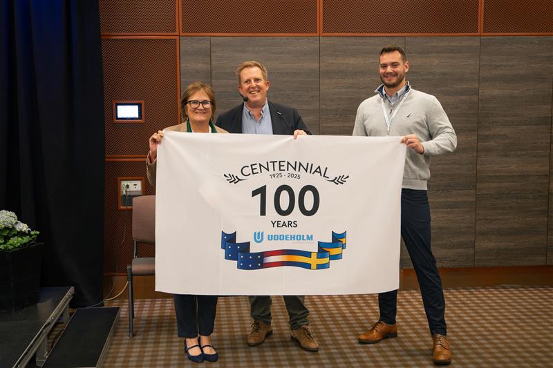 Three people holding a flag with the text 100 years Uddeholm