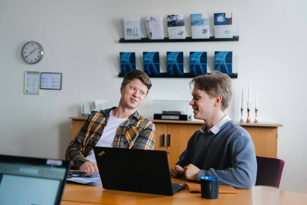 two men sitting at a table with a laptop