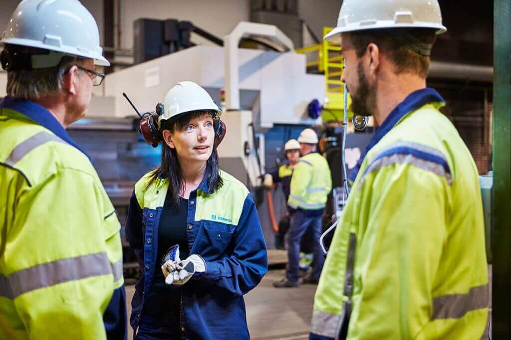 three steel plant workers wearing protective gear are talking to each other