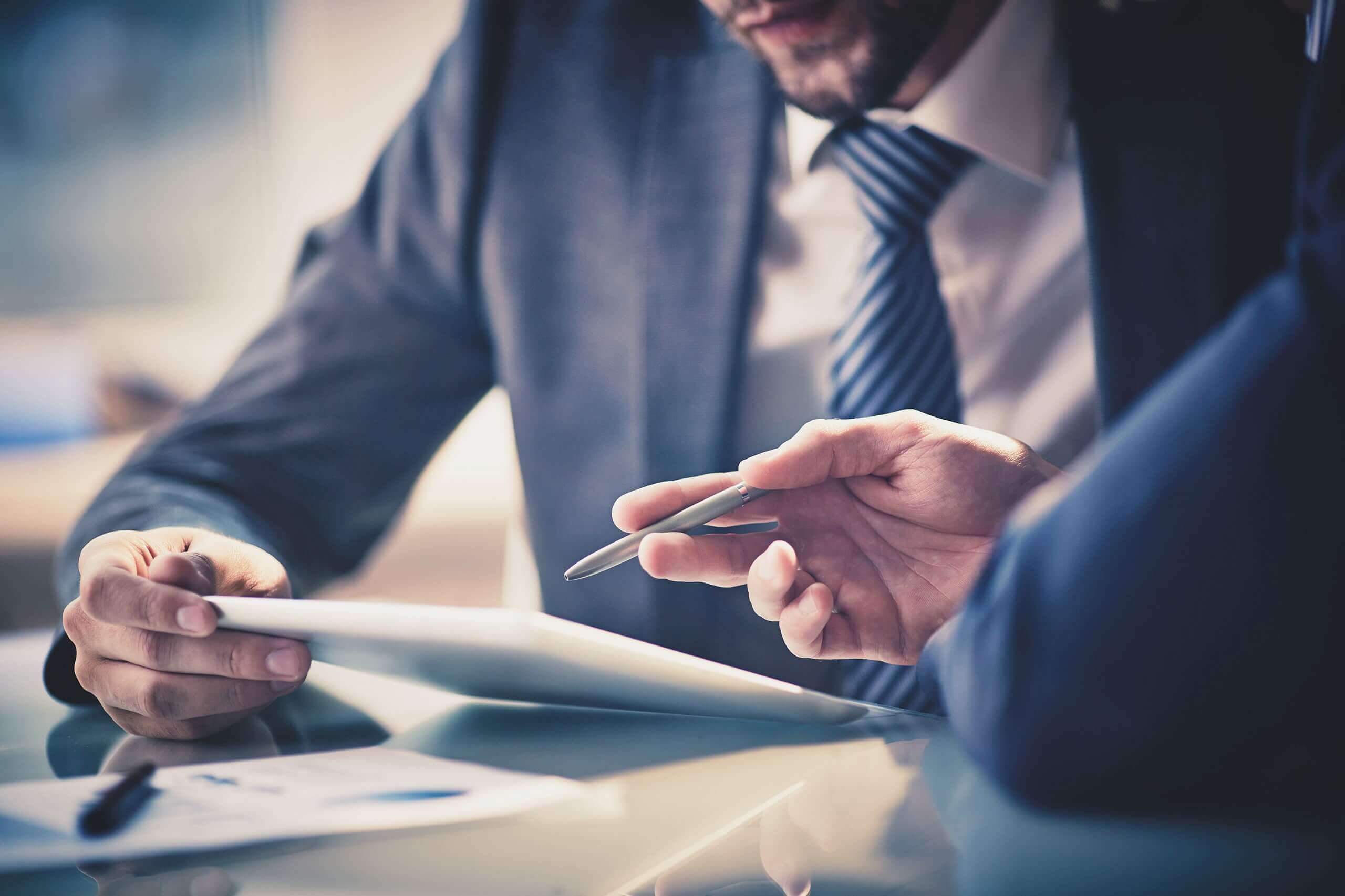 Primer plano de dos personas vestidas de negocios mirando una pantalla de tableta y discutiendo.